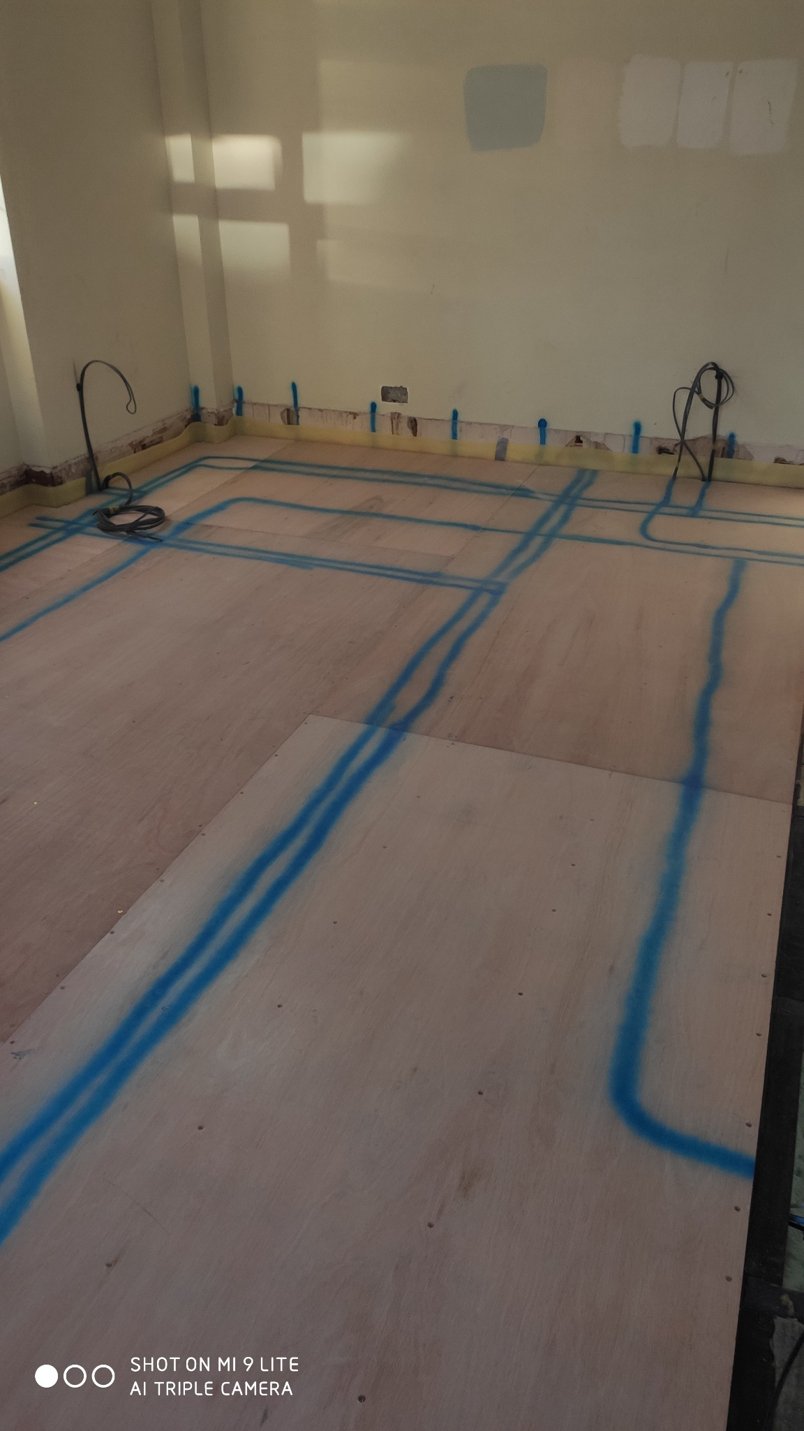 Przygotowanie podłoża pod panele: Płyta OSB z wyrysowanymi niebieską farbą liniami instalacji elektrycznej, widoczne kable w rogu pomieszczenia.