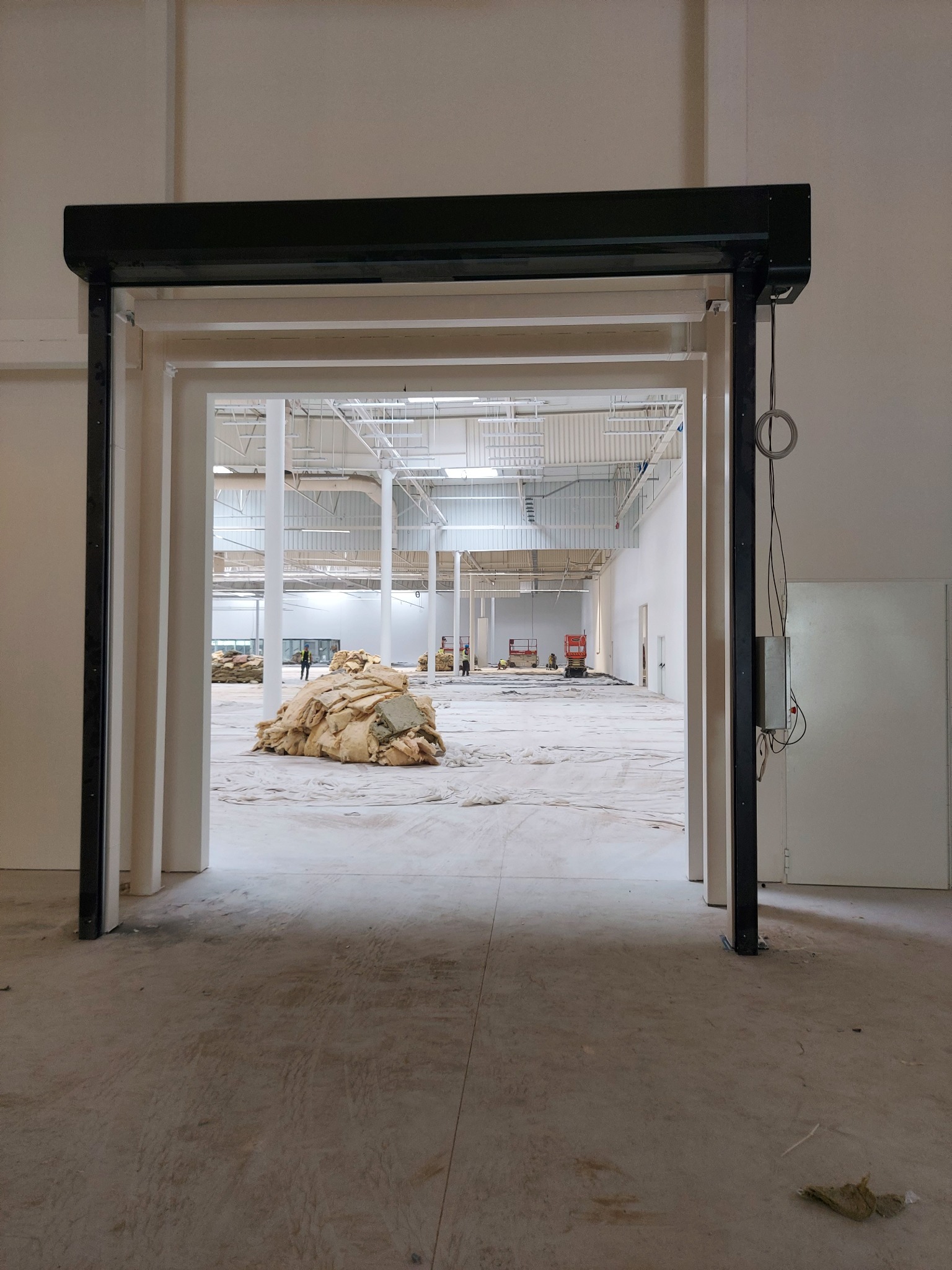 Otwarta brama przemysłowa w hali magazynowej, widoczne materiały izolacyjne i pracownicy w oddali.