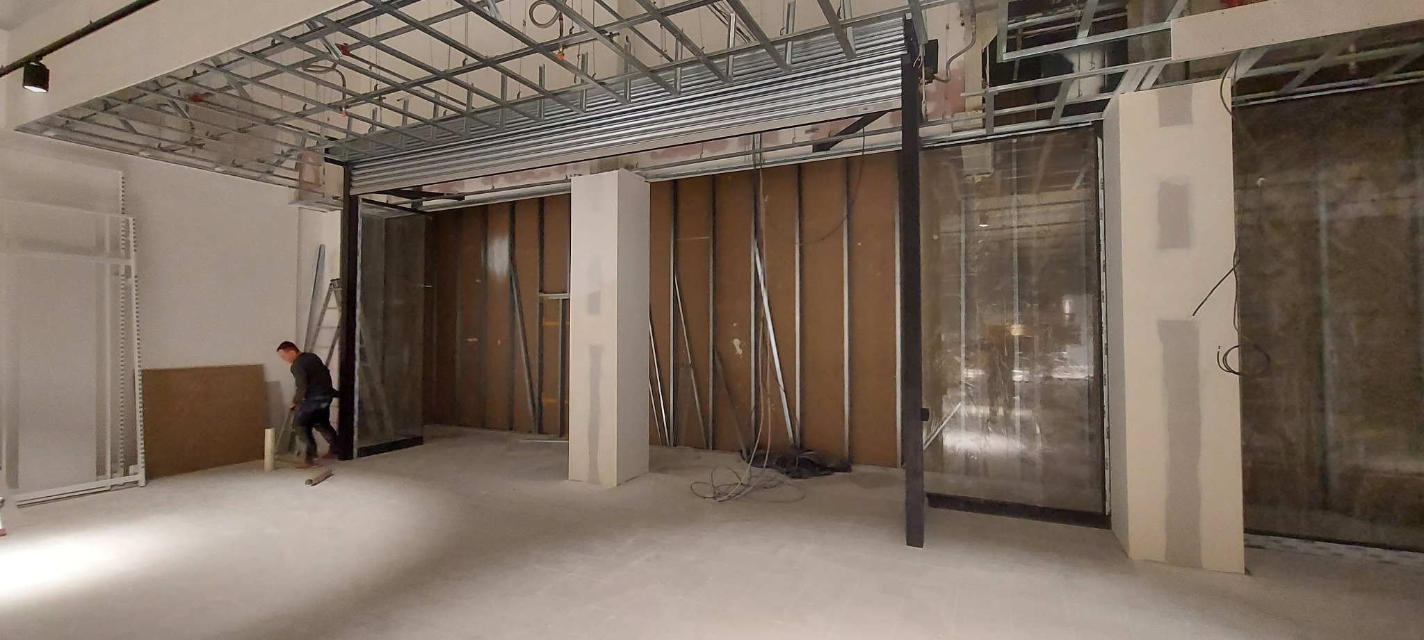 Montaż stalowej konstrukcji sufitowej i ścian działowych w lokalu, widoczna osoba sprzątająca podłogę.