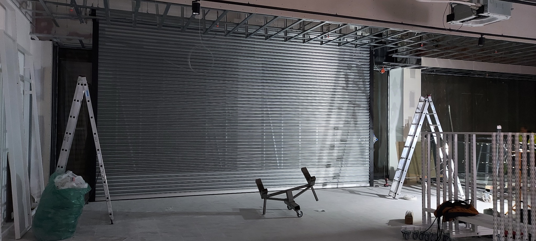 Zamknięta, metalowa kurtyna w hali produkcyjnej, widoczne drabiny i elementy konstrukcyjne sufitu.