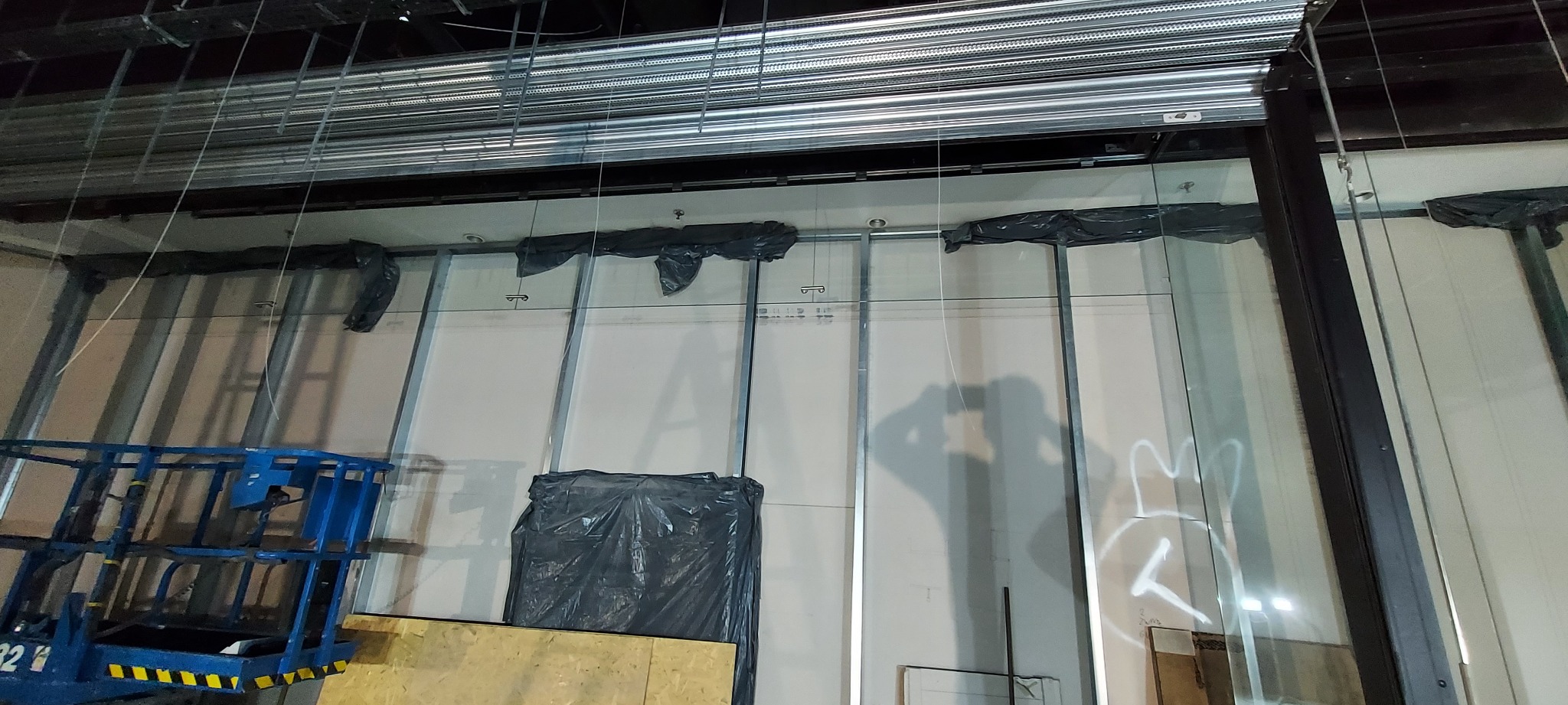 Montaż konstrukcji stalowej z elementami zabezpieczonymi folią, widoczny podnośnik koszowy i instalacje pod sufitem.