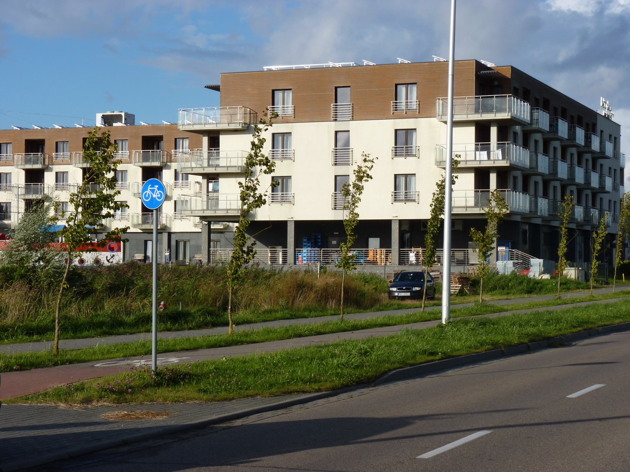Widok zewnętrzny budynku hotelu Baltic Plaza w Kołobrzegu z elementami nowoczesnej architektury, widoczny znak ścieżki rowerowej.