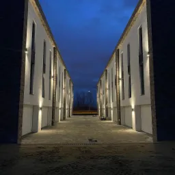 Rząd nowo wybudowanych szeregowców z oświetleniem zewnętrznym, sfotografowany o zmierzchu, z widocznym placem budowy przed budynkami.