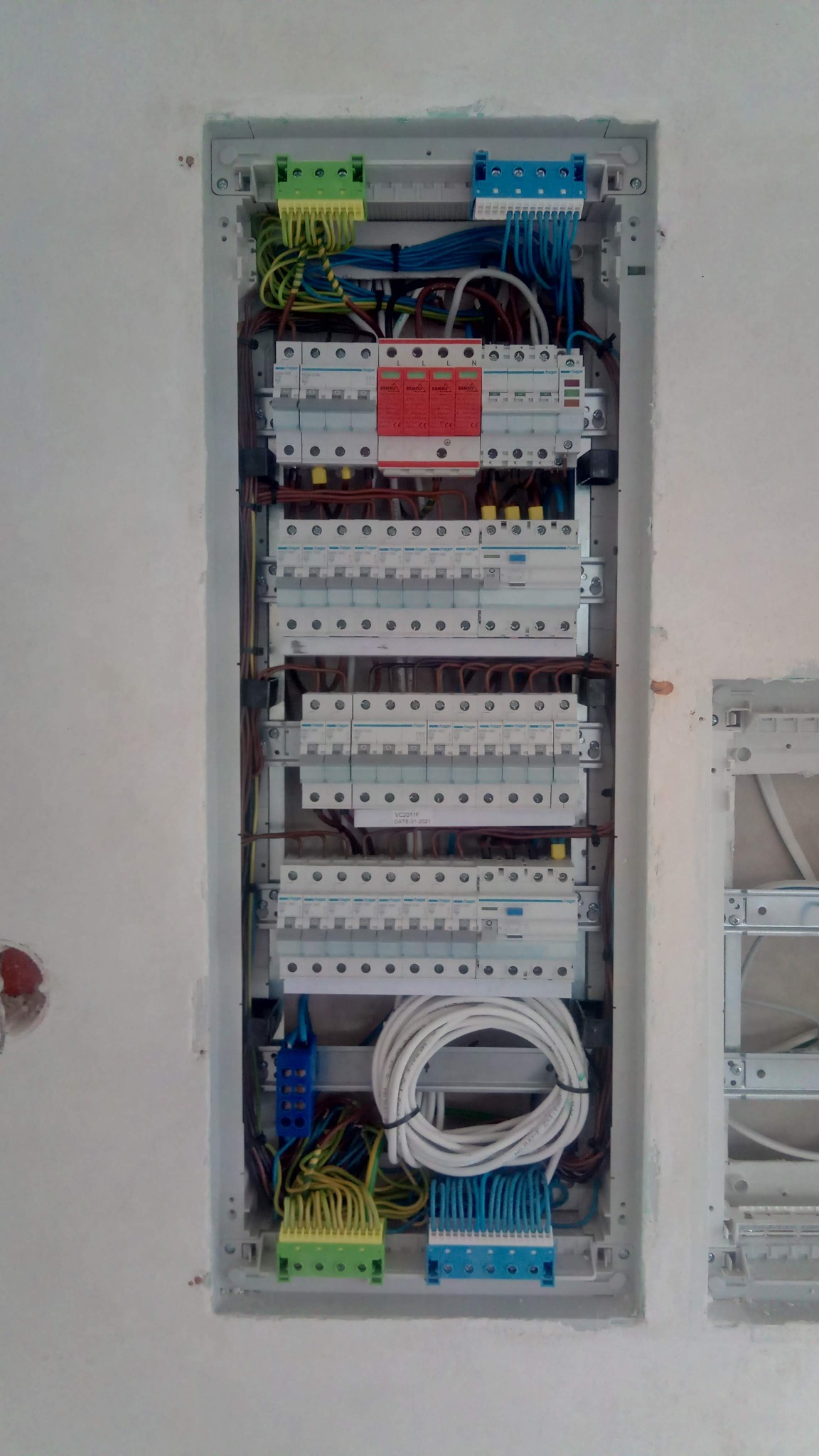 Rozdzielnica elektryczna wnękowa z widocznymi zabezpieczeniami, przewodami i listwami zaciskowymi, zamontowana w surowej ścianie.