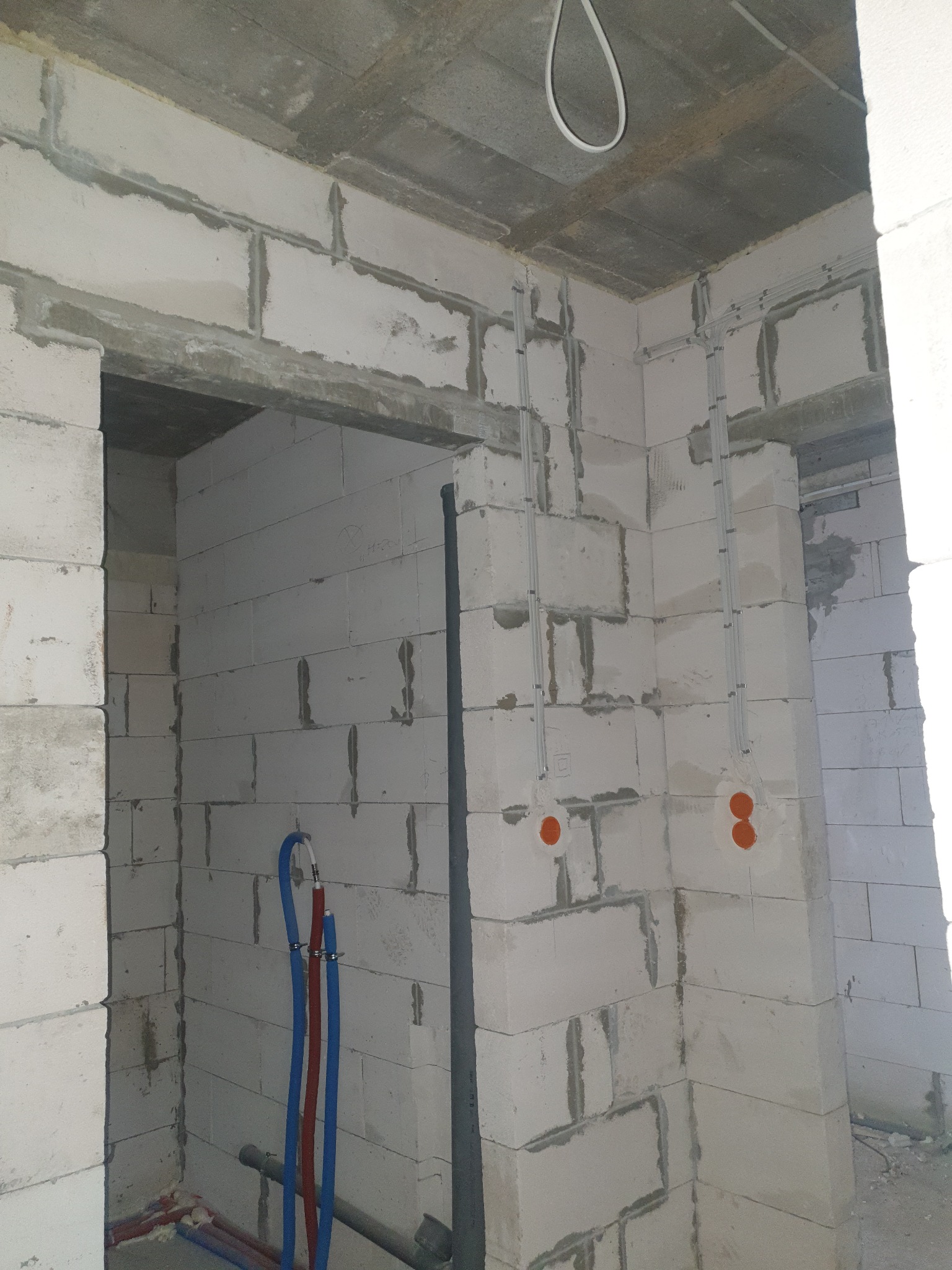 Surowy stan: instalacja elektryczna i rury w ścianach z betonu komórkowego przed wykończeniem. Widoczne kable i puszki elektryczne oraz rury wodne.