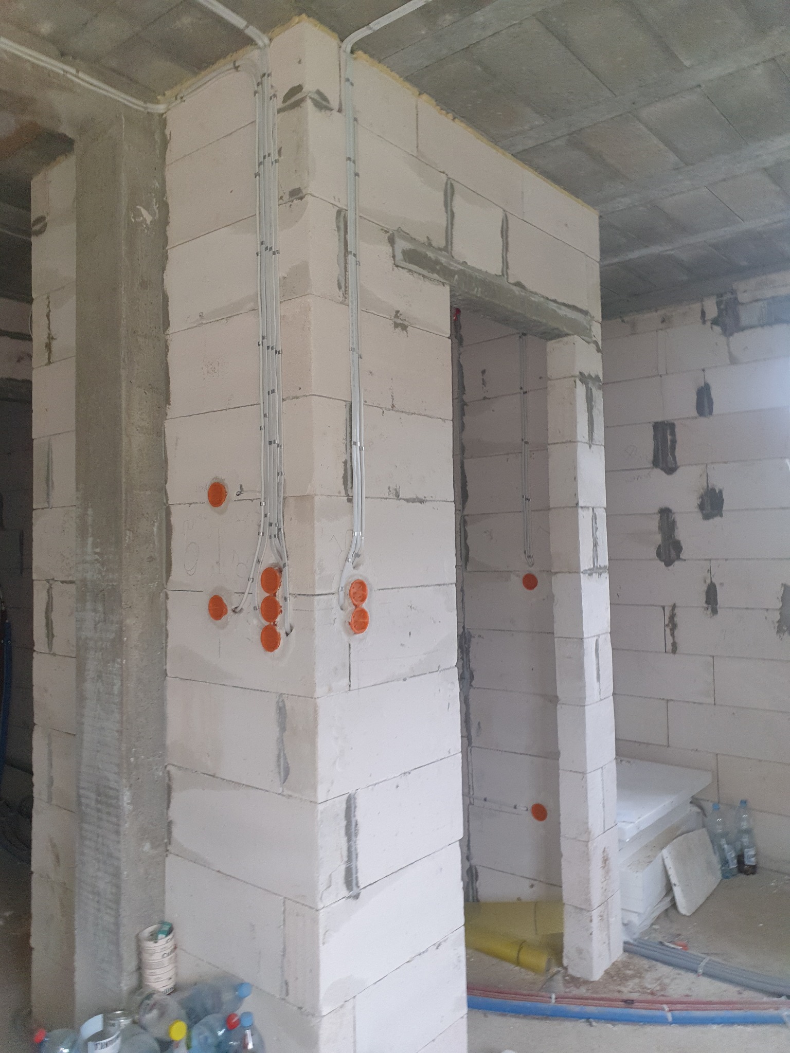 Surowy stan: instalacja elektryczna w bruzdach ścian z betonu komórkowego, widoczne puszki i peszle. Przewody prowadzone wzdłuż ścian i pod stropem.