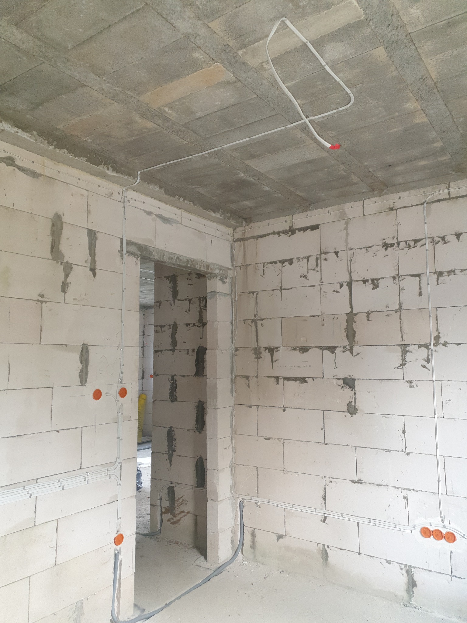 Surowy stan instalacji elektrycznej w budynku w Niemcach: kable i puszki podtynkowe na ścianach z betonu komórkowego, widok na sufit z przewodami.