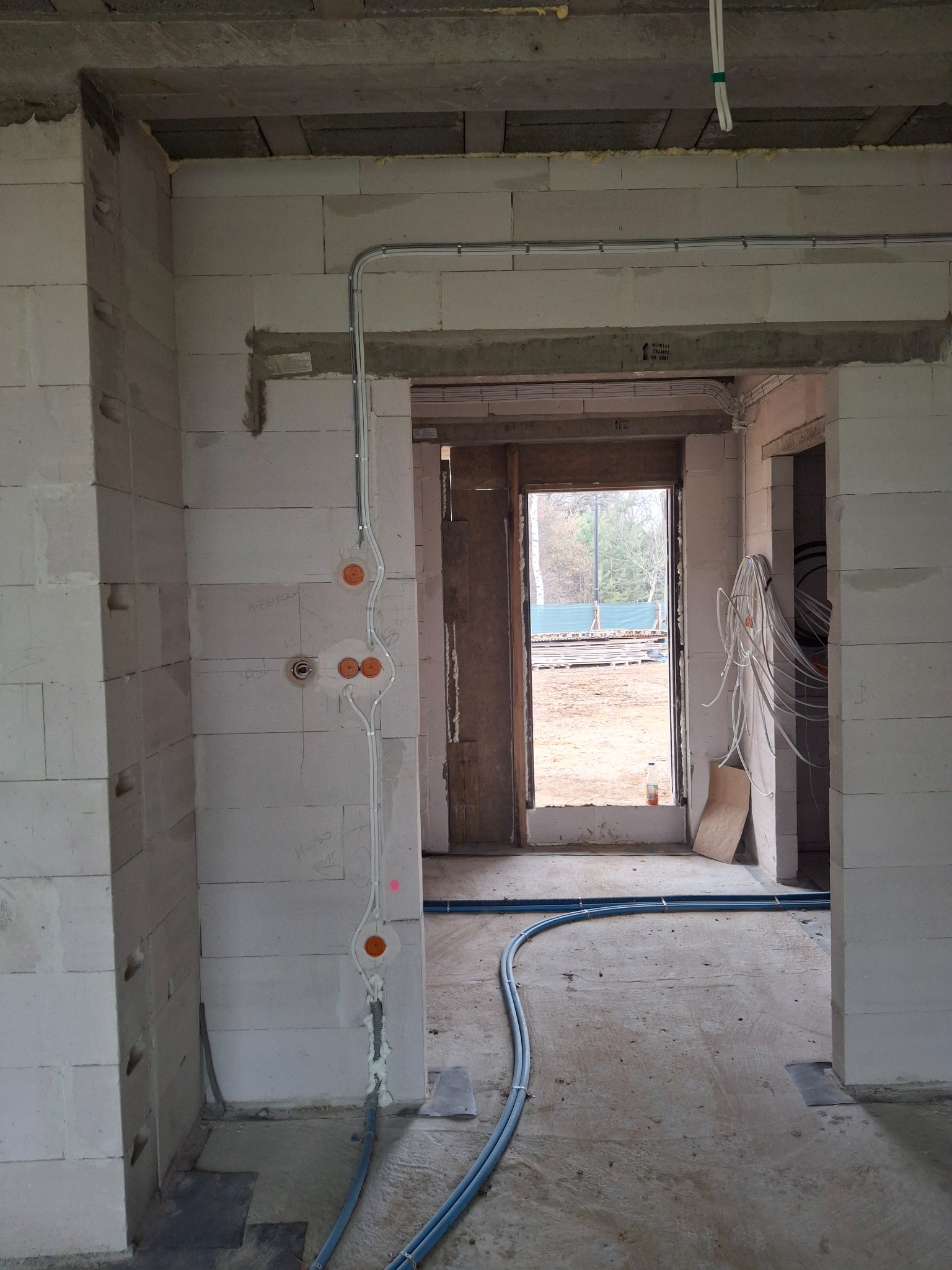 Wewnętrzne okablowanie w surowym budynku z białych bloków, widoczne rury i puszki instalacyjne, przygotowane do dalszych prac wykończeniowych.