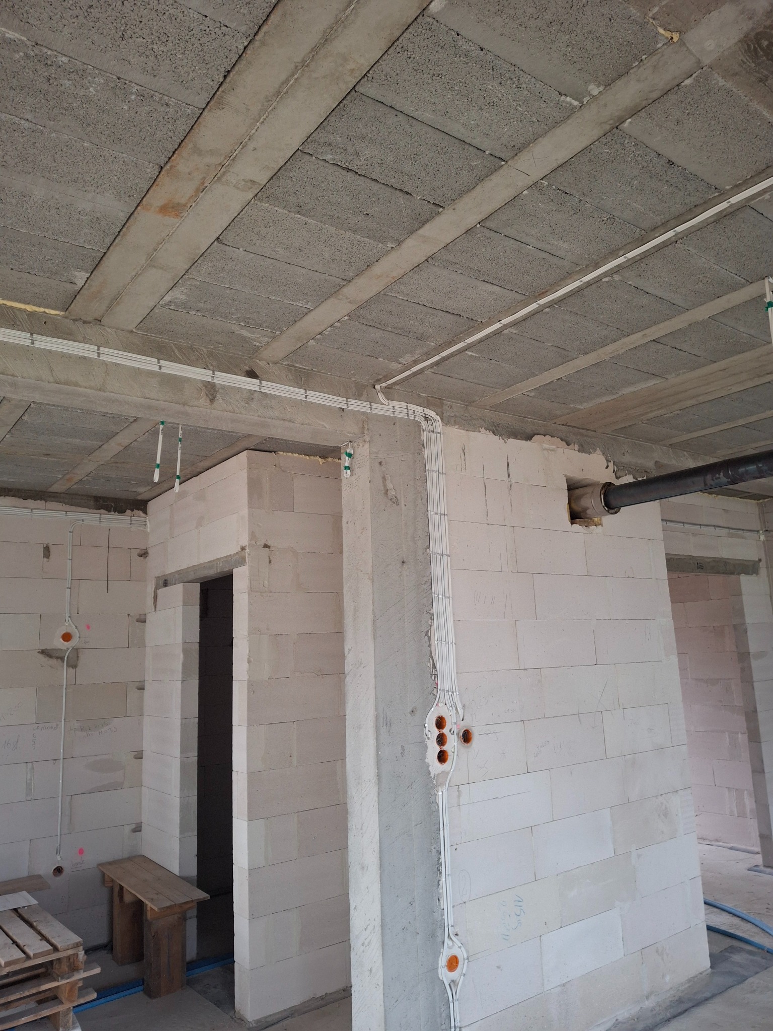 Wewnętrzne ściany z betonu komórkowego w trakcie instalacji elektrycznej: kable prowadzone w bruzdach, puszki pod gniazdka. Widoczny surowy strop i fragment instalacji wentylacyjnej.