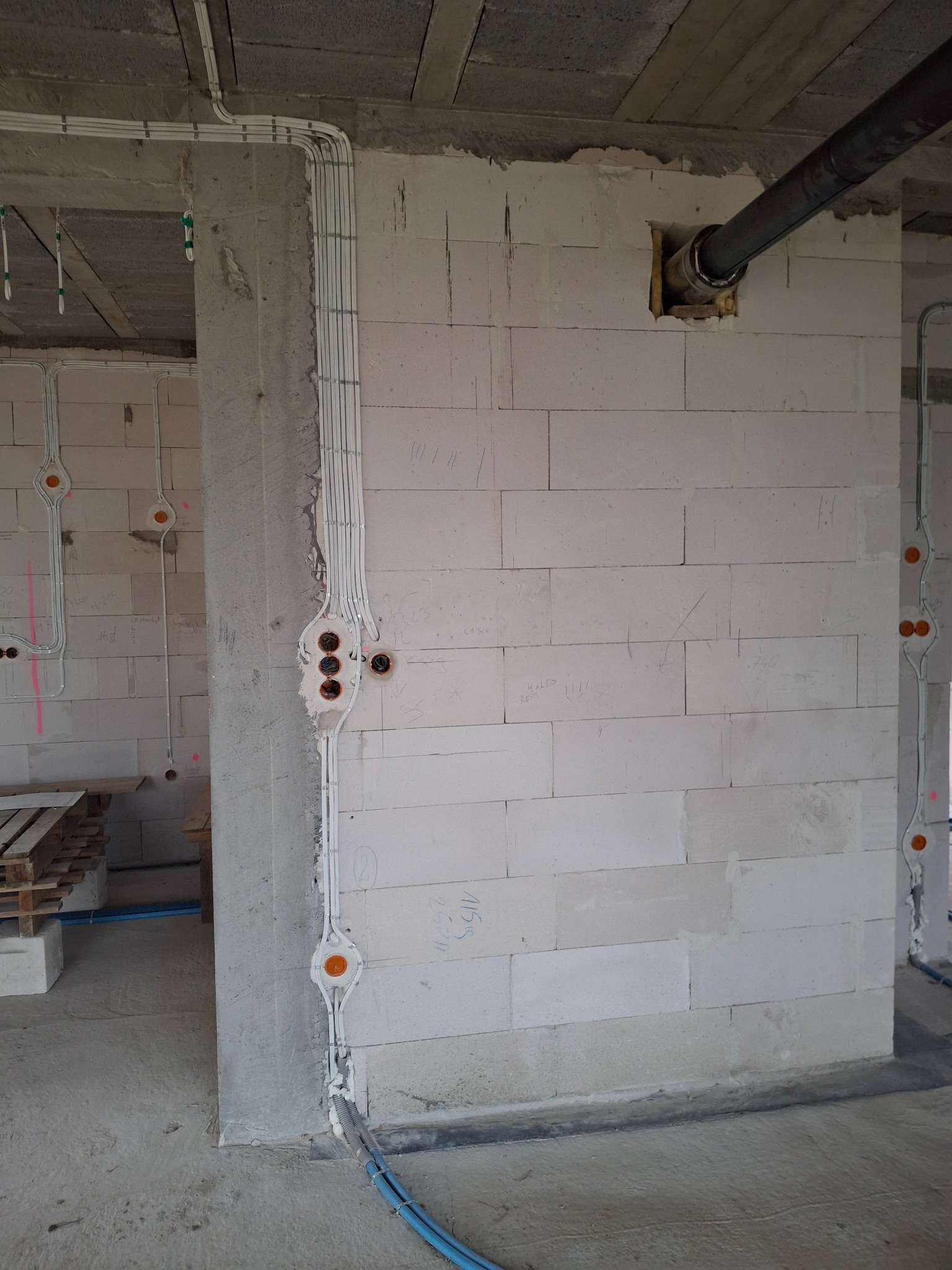 Surowe ściany z betonu komórkowego z widoczną, częściowo zamontowaną instalacją elektryczną w peszlach i puszkach. Widoczne przewody w kolorze niebieskim.