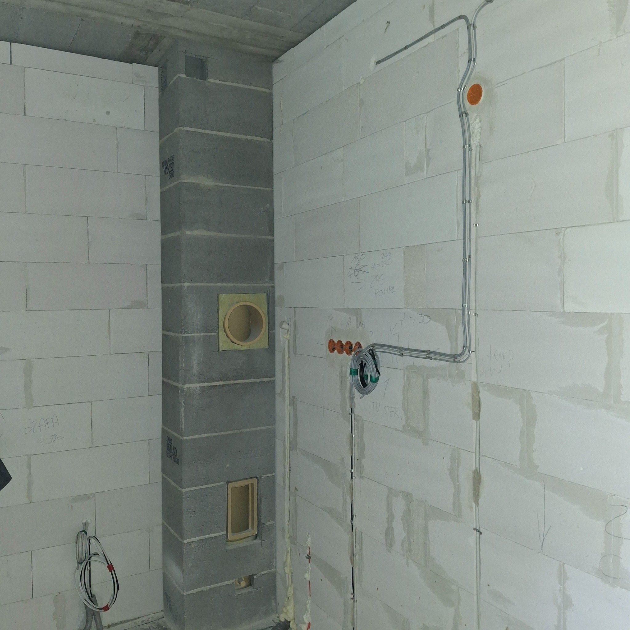 Instalacja elektryczna w surowym wnętrzu w Niemcach: kable w peszlach prowadzone po ścianie z bloczków, puszki instalacyjne, otwory w kominie. Etap prac.