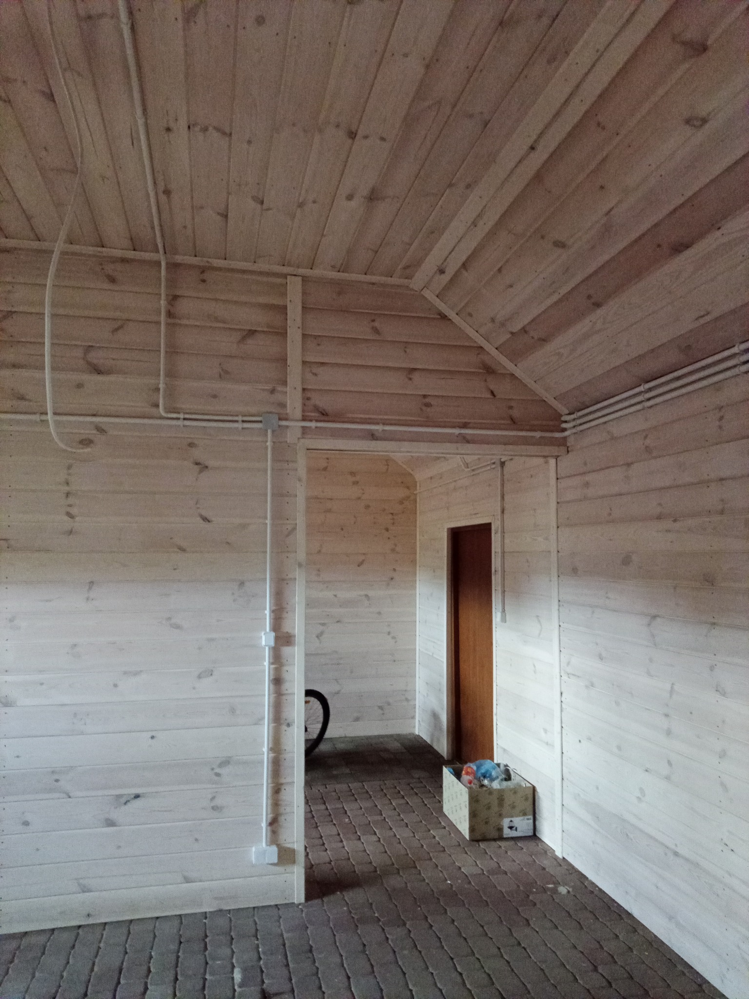 Wnętrze drewnianej konstrukcji z widocznymi przewodami elektrycznymi poprowadzonymi po ścianach i suficie, skrzynka z narzędziami i fragment roweru w tle.