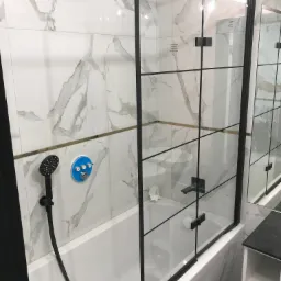 Nowoczesna kabina prysznicowa z czarnymi profilami i armaturą, marmurowe płytki na ścianach, bateria z niebieskim panelem sterowania.
