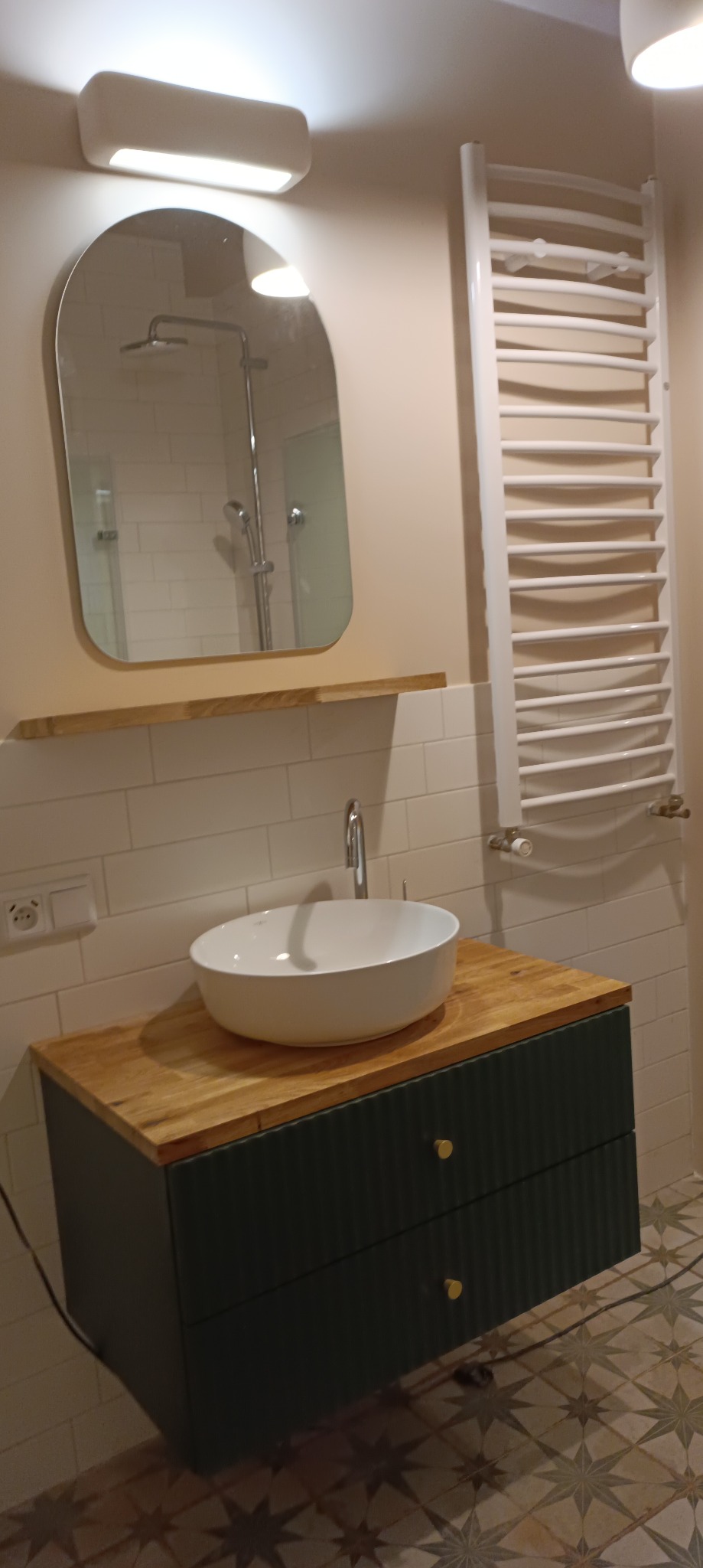 Nowoczesna łazienka po remoncie: biała umywalka nablatowa na szafce z frezowanymi frontami w kolorze butelkowej zieleni, drewniany blat, białe płytki na ścianach, lustro w zaokrąglonej ramie...