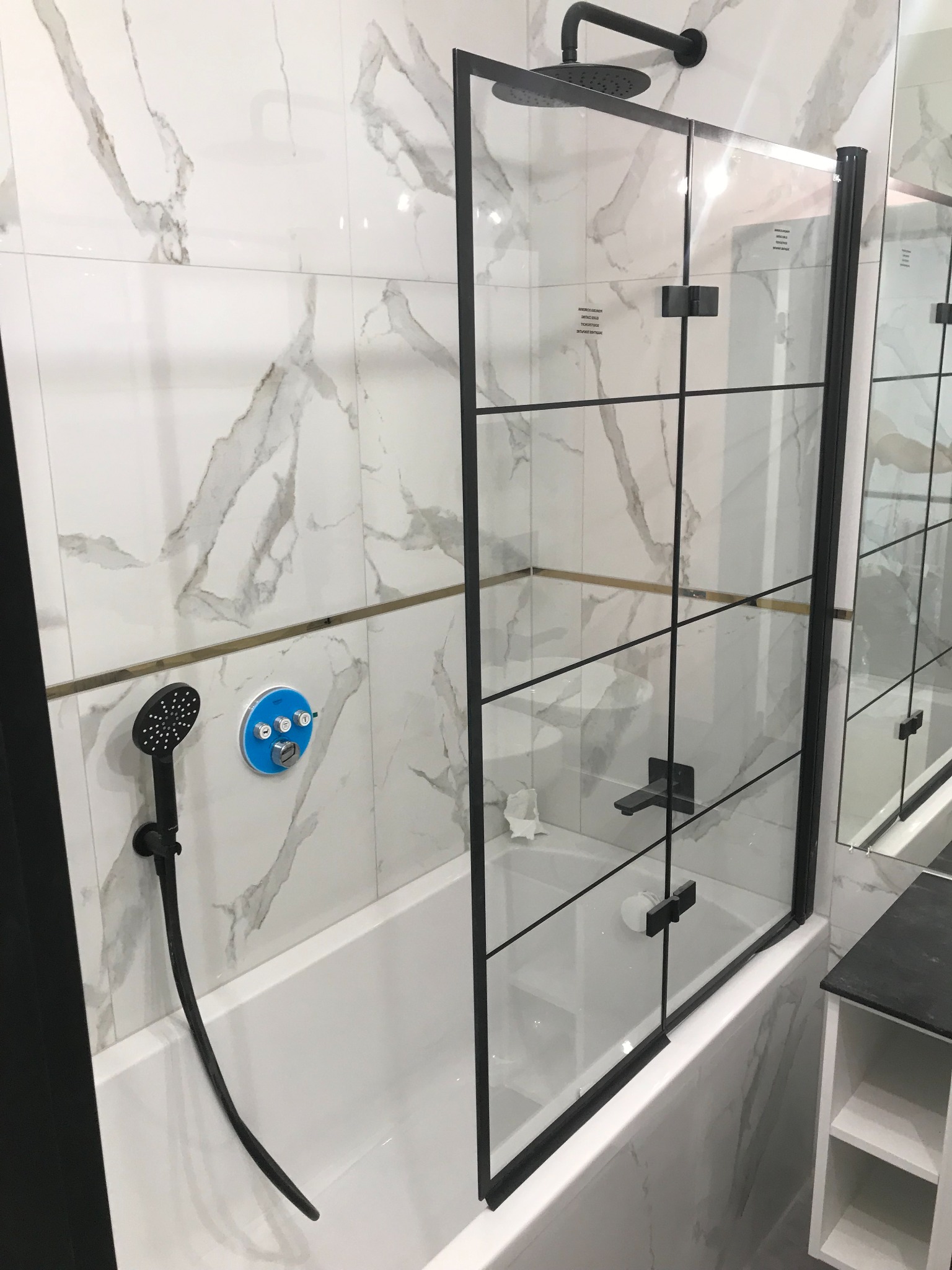 Nowoczesna kabina prysznicowa z czarnymi profilami i armaturą, marmurowe płytki na ścianach, bateria z niebieskim panelem sterowania.