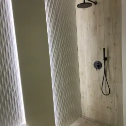 Nowoczesna kabina prysznicowa z drewnopodobnymi płytkami, czarną armaturą i dekoracyjnymi panelami 3D z podświetleniem LED.