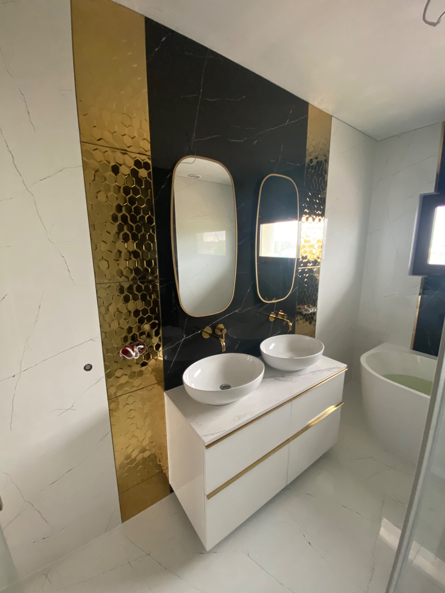 Nowoczesna łazienka z umywalkami nablatowymi, złotymi akcentami i płytkami imitującymi marmur oraz plastry miodu.