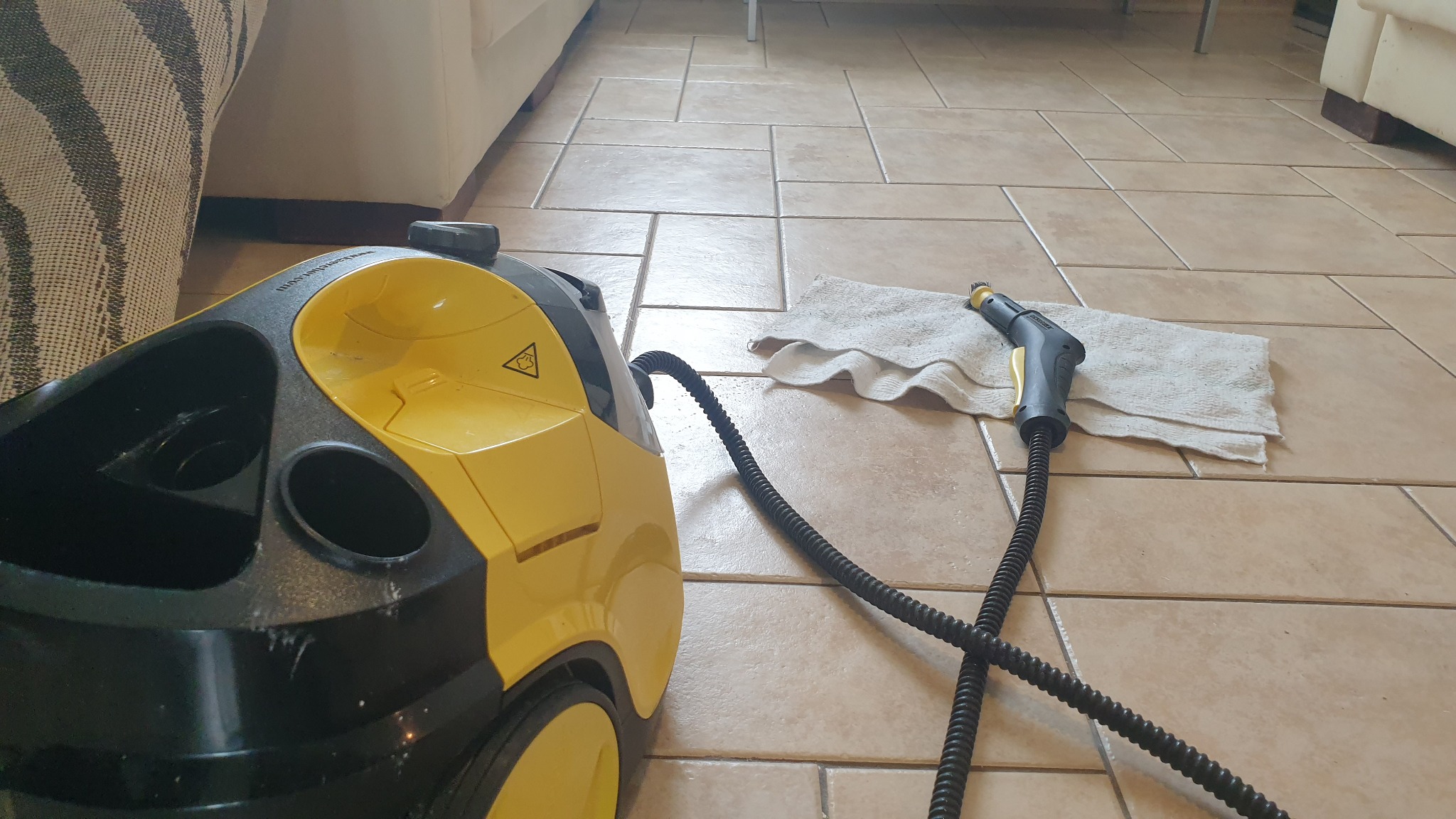 Żółto-czarny parowy odkurzacz Karcher z dyszą i białą ściereczką na beżowych płytkach podłogowych, widok z góry.