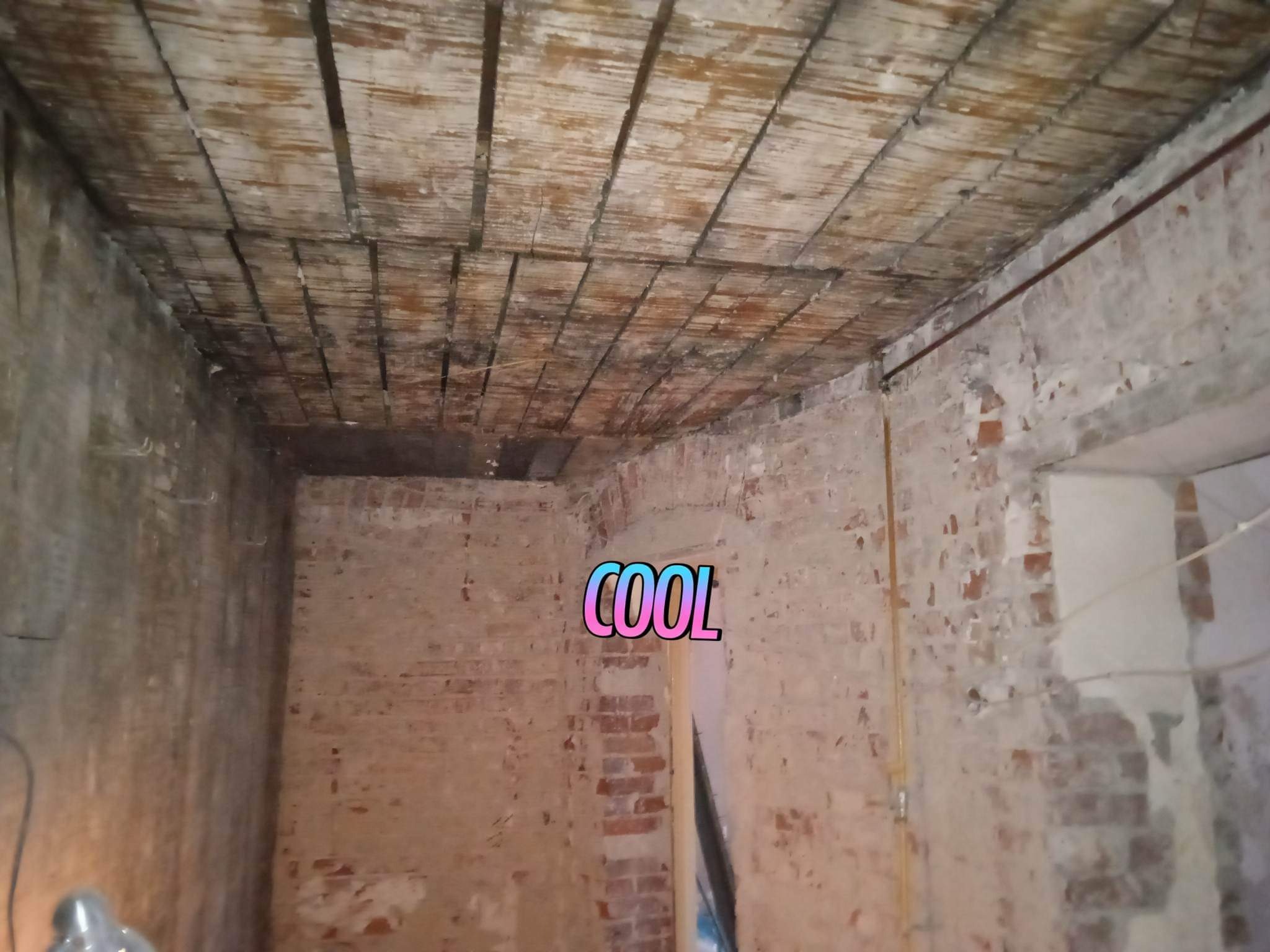 Wnętrze starego budynku z odsłoniętą cegłą i drewnianym sufitem w trakcie prac remontowych, widoczne ślady po skuciu tynku.