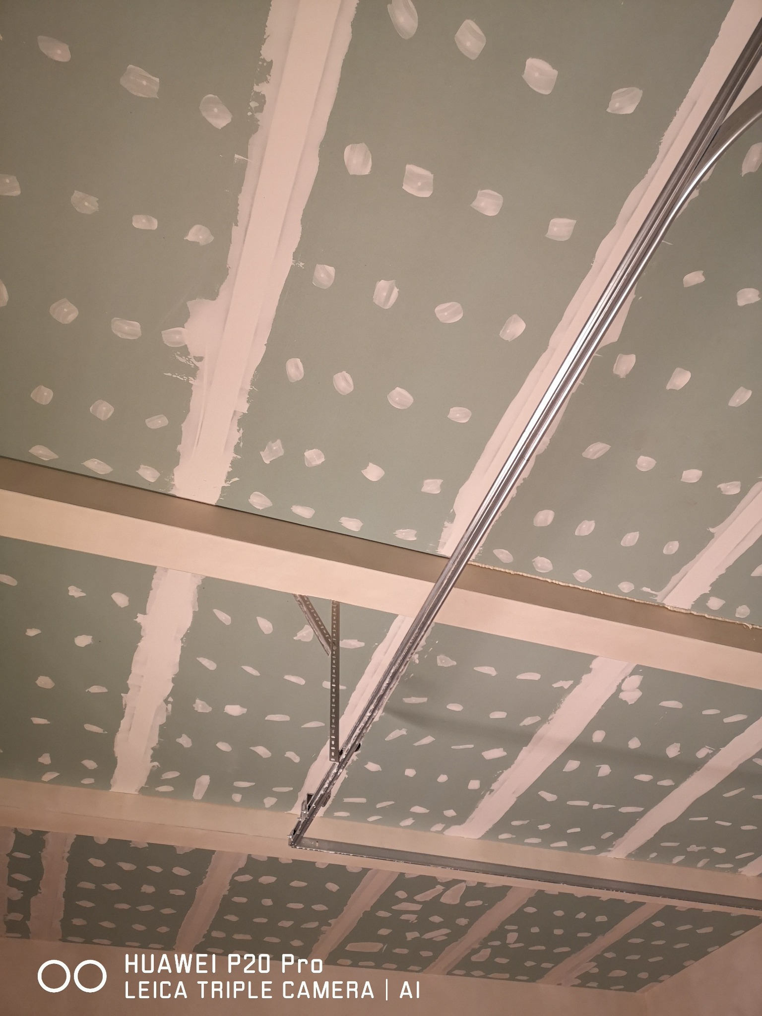 Sufit z płyt kartonowo-gipsowych w trakcie montażu, widoczne profile metalowe i łączenia płyt zaszpachlowane punktowo, surowy stan przed finalnym wykończeniem.