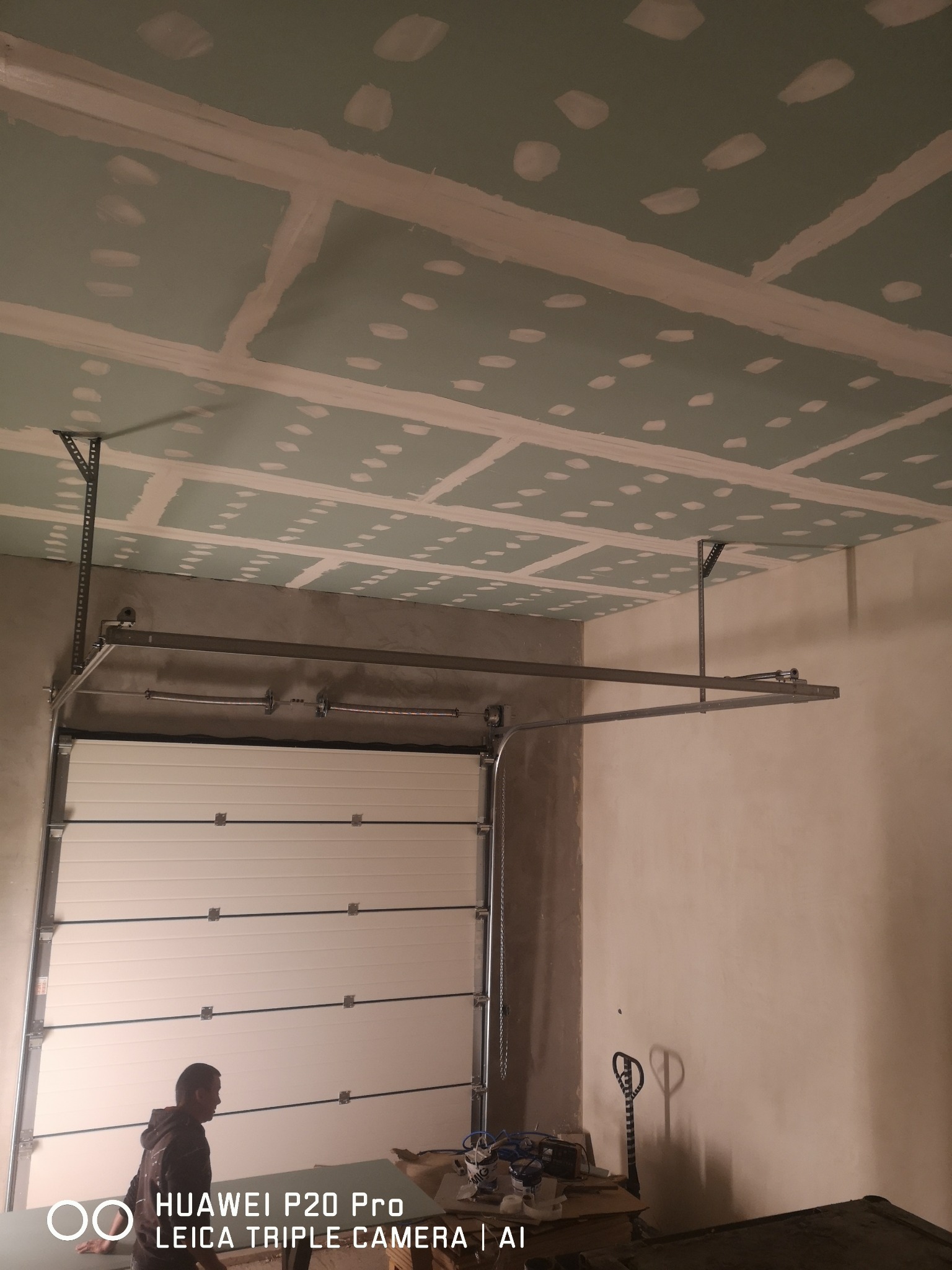 Montaż sufitu z płyt karton-gips w garażu z widocznym systemem mocowania i częściowo otwartą bramą garażową.