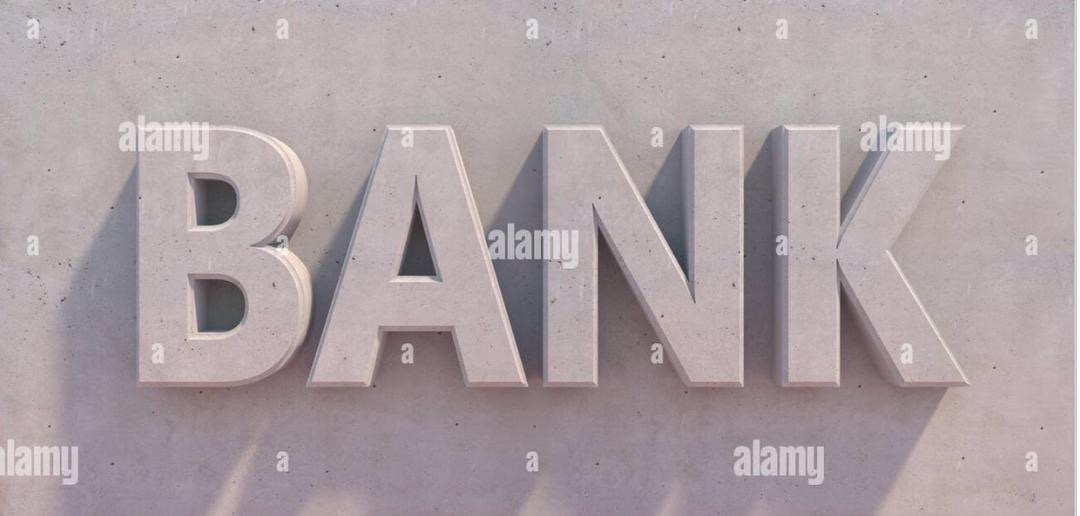 Betonowy napis 'BANK' na szarej, teksturowanej ścianie z delikatnym cieniem, sugerujący stabilność finansową.