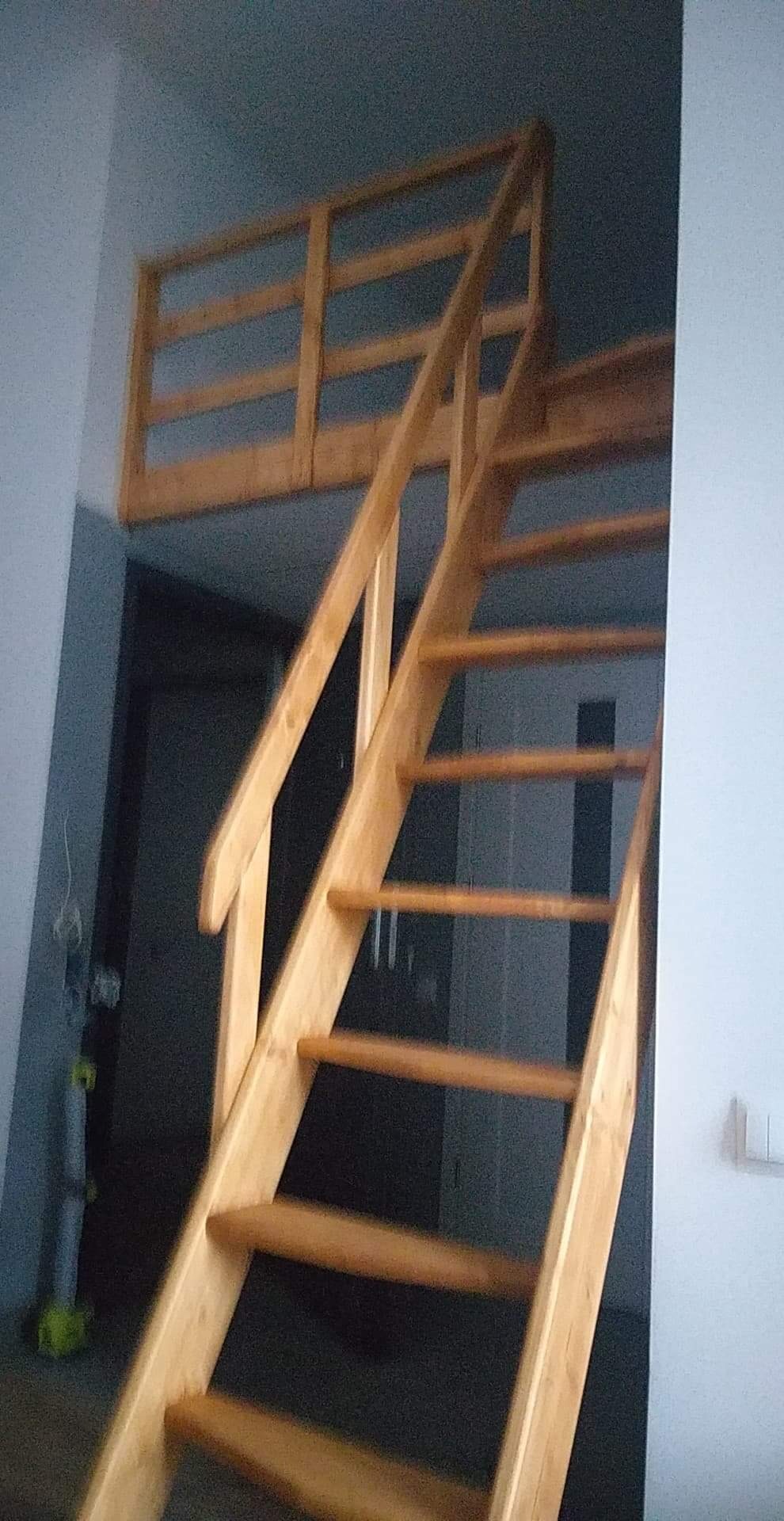 Drewniane schody prowadzące na antresolę z drewnianą balustradą, widoczne jasne drewno i surowe wykończenie wnętrza.