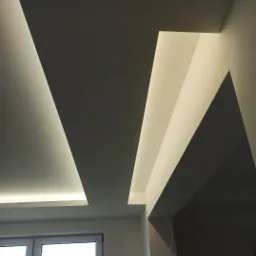 Nowoczesny sufit podwieszany z oświetleniem LED w kształcie geometrycznym, widoczne okno w tle.