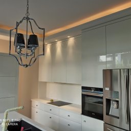 Artur kułak wykończenia wnętrz - Nowoczesna kuchnia z białymi, lakierowanymi szafkami, chromowanym oświetleniem i sprzętem AGD ze stali nierdzewnej, widok na sufit z oświetleniem LED.