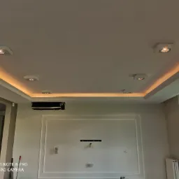 Kasetonowy sufit podwieszany z oświetleniem LED i punktowymi lampami w nowoczesnym salonie, widoczne elementy dekoracyjne ścian i klimatyzacja.