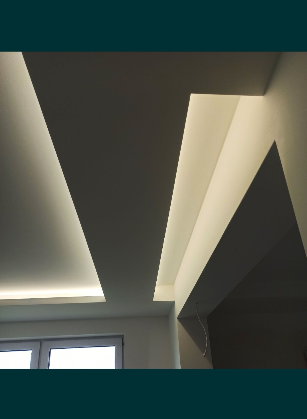 Nowoczesny sufit podwieszany z oświetleniem LED w kształcie geometrycznym, widoczne okno w tle.