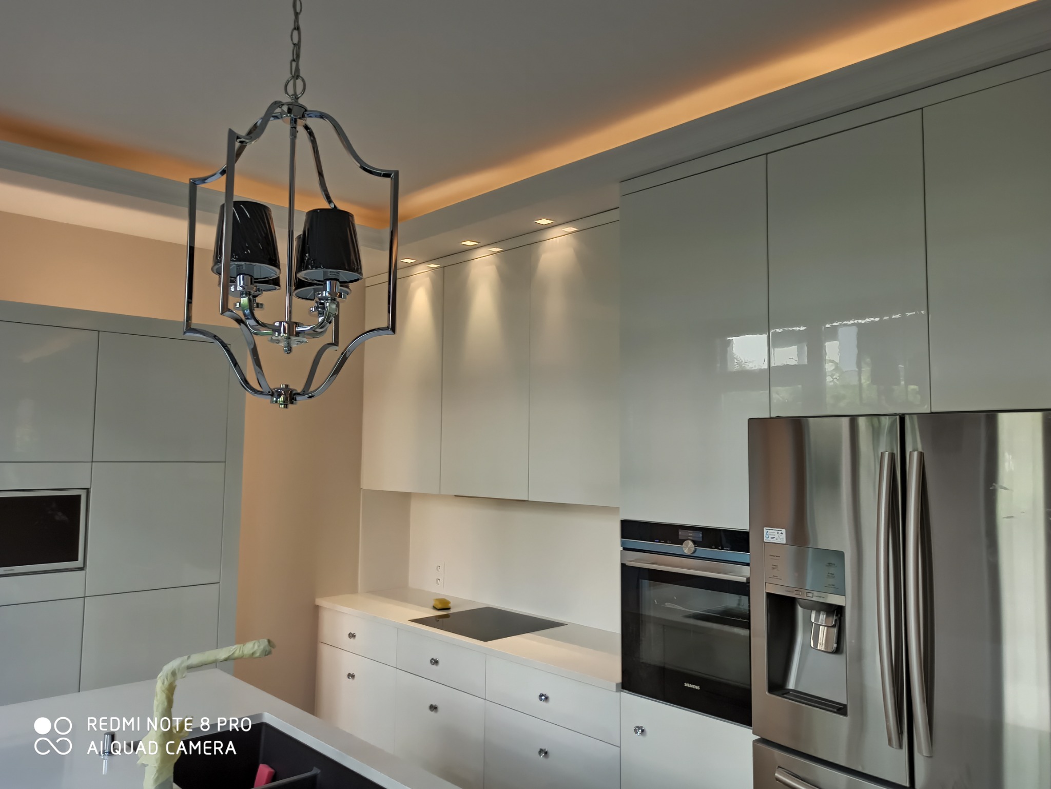 Nowoczesna kuchnia z białymi, lakierowanymi szafkami, chromowanym oświetleniem i sprzętem AGD ze stali nierdzewnej, widok na sufit z oświetleniem LED.