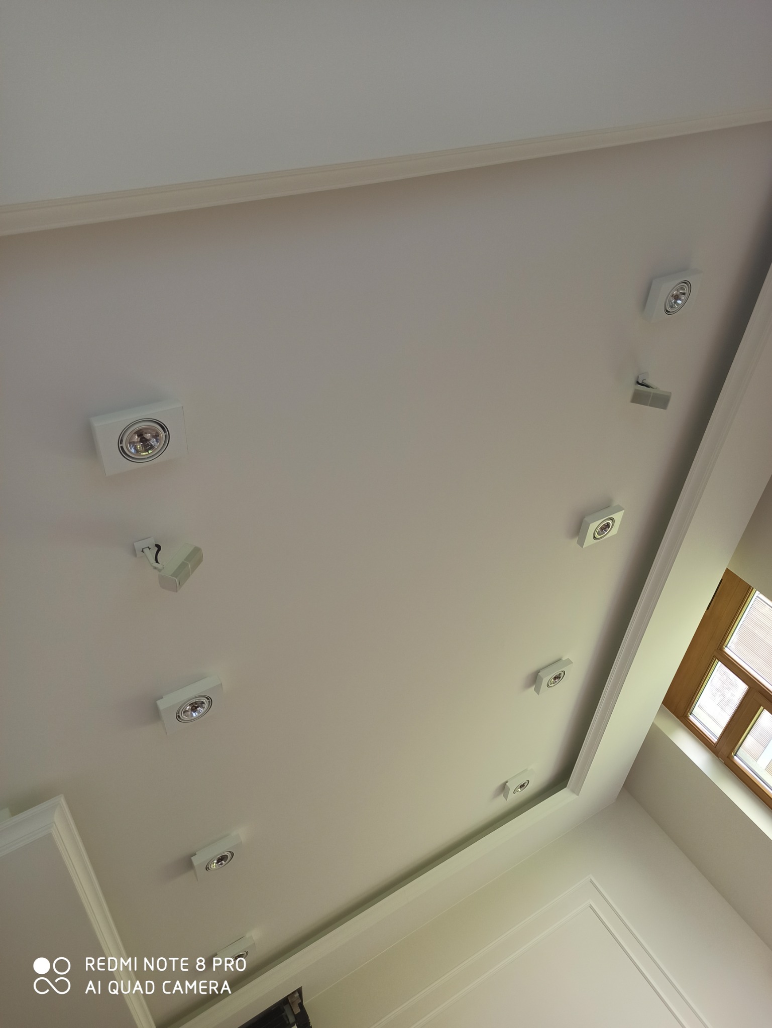 Biały sufit z zamontowanymi, kwadratowymi lampami punktowymi w Radzyniu Podlaskim, widok z dołu, obok okno z drewnianą ramą.