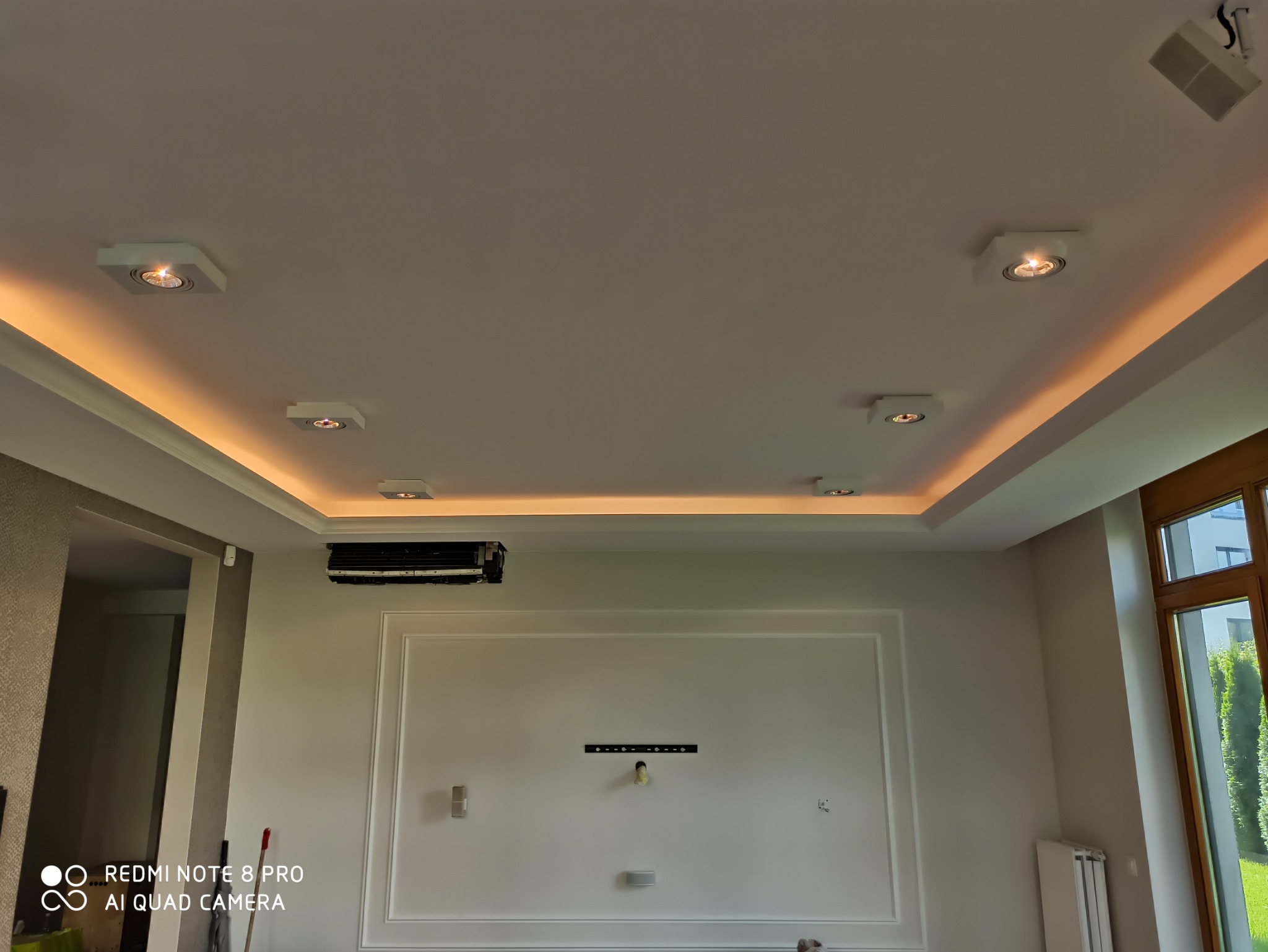 Kasetonowy sufit podwieszany z oświetleniem LED i punktowymi lampami w nowoczesnym salonie, widoczne elementy dekoracyjne ścian i klimatyzacja.