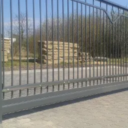 Nowoczesna, przesuwna brama panelowa z automatyką BFT, zamontowana przy posesji z kamiennym ogrodzeniem. Widoczne elementy konstrukcyjne i mechanizm napędowy.