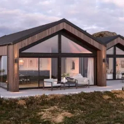 Nowoczesny, dwusegmentowy budynek z drewnianą elewacją i dużymi przeszkleniami, otoczony naturalnym krajobrazem z widocznymi skałami.