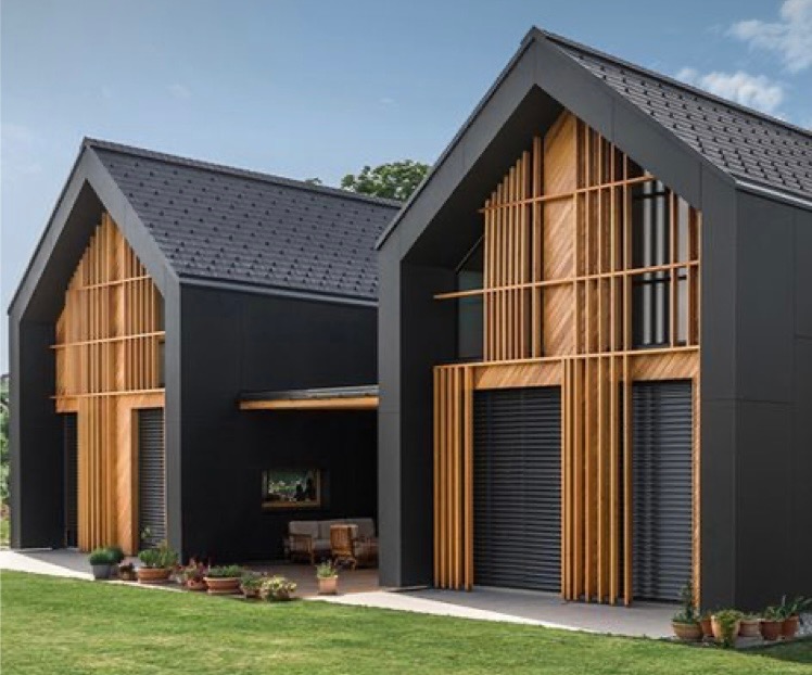 Dwa nowoczesne domy szkieletowe o czarnych ścianach i drewnianych elementach fasady, grafitowy dach, zielony trawnik z doniczkami przed domem.