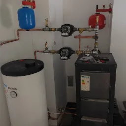 Kotłownia w Kobylcu z piecem na paliwo stałe, zasobnikiem ciepłej wody marki Kospel, pompami obiegowymi i naczyniami wzbiorczymi, widoczne narzędzia na górnej części kotła.