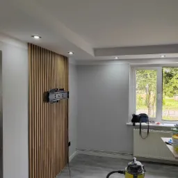 Nowoczesny salon z drewnianą ścianką działową z listew, uchwytem na telewizor i odkurzaczem po remoncie