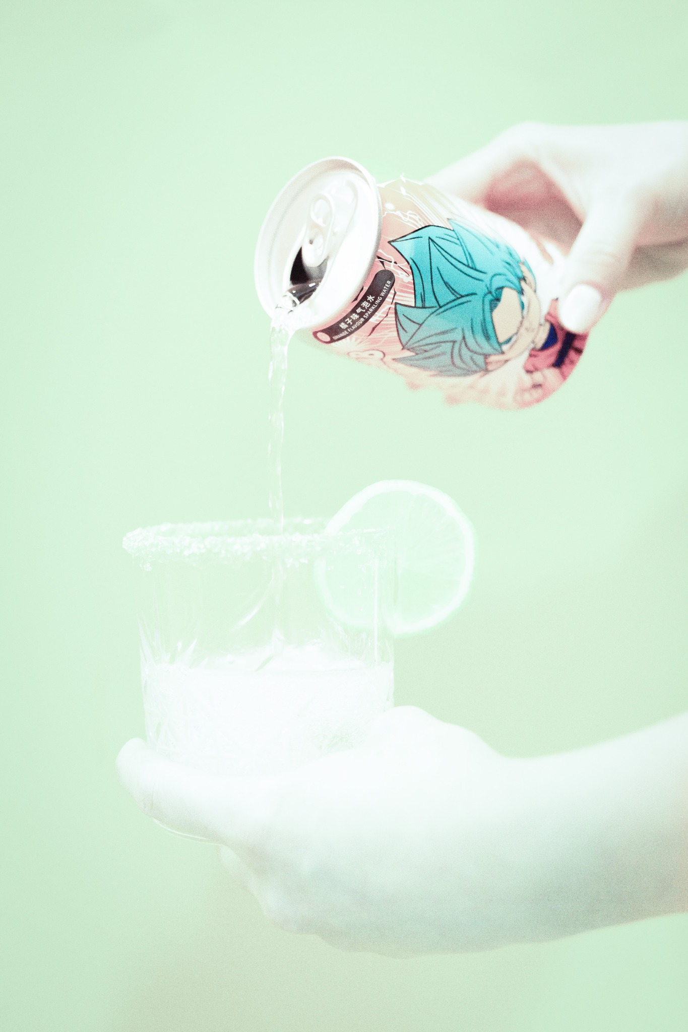 Nalewanie napoju z puszki z motywem anime do szklanki z plasterkiem limonki i obwódką z kryształków, na jasnym tle.