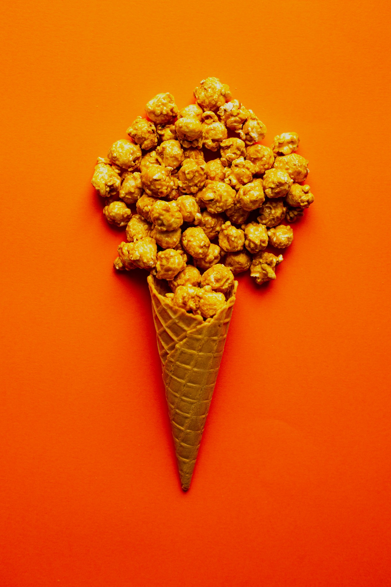 Karmelowy popcorn w wafelku na pomarańczowym tle, ułożony w kształt lodów.