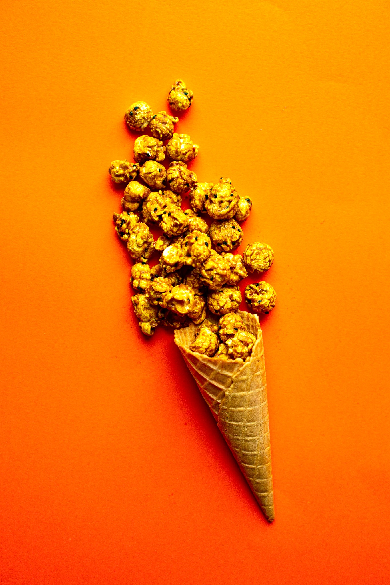 Karmelowy popcorn wysypujący się z wafelka na pomarańczowym tle, ujęcie z góry.