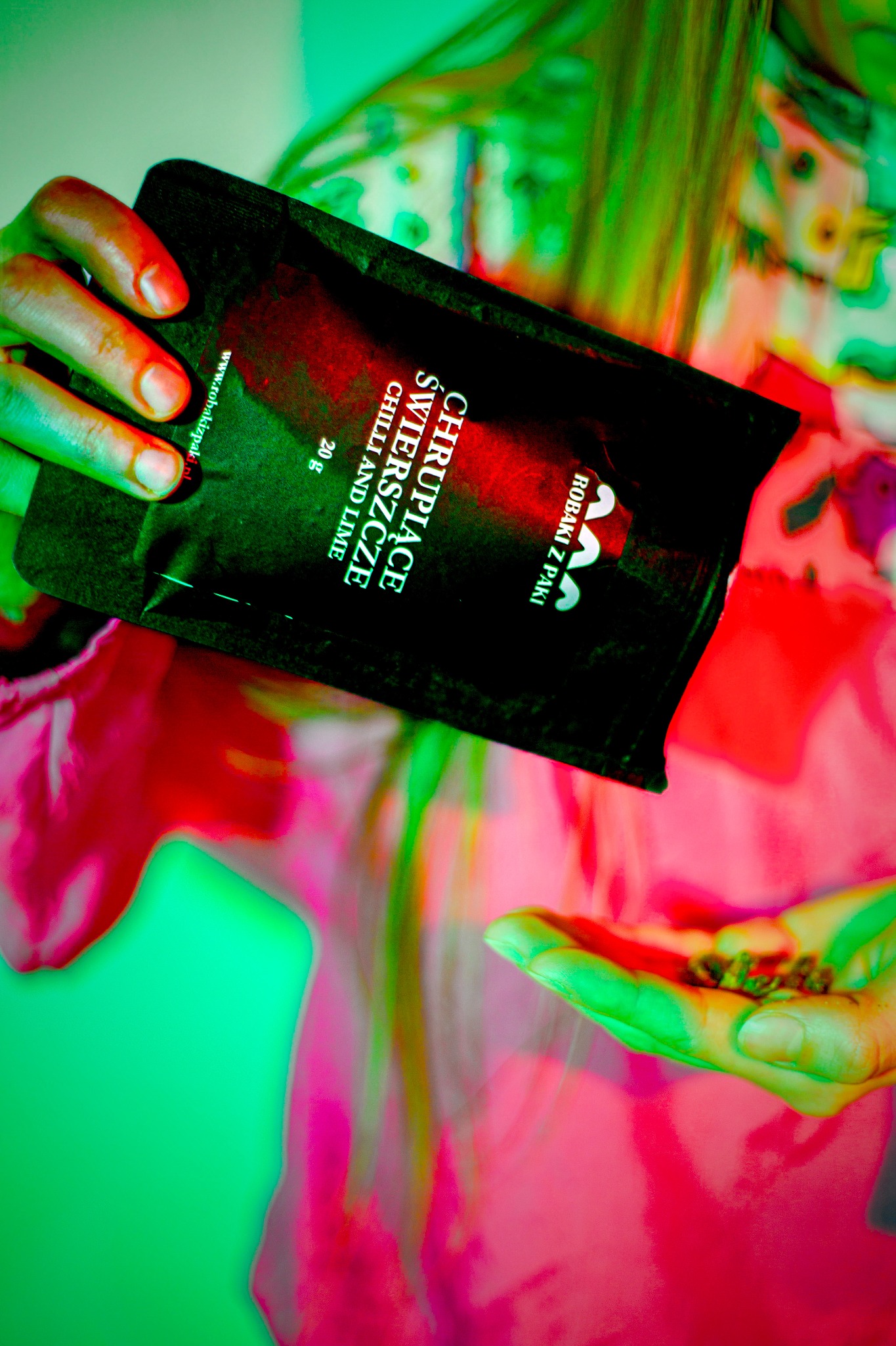 Osoba przesypuje zawartość czarnej paczki z napisem 'Chrupiące Świeższe Chilli and Lime' do dłoni, widoczne małe brązowe kawałki produktu.