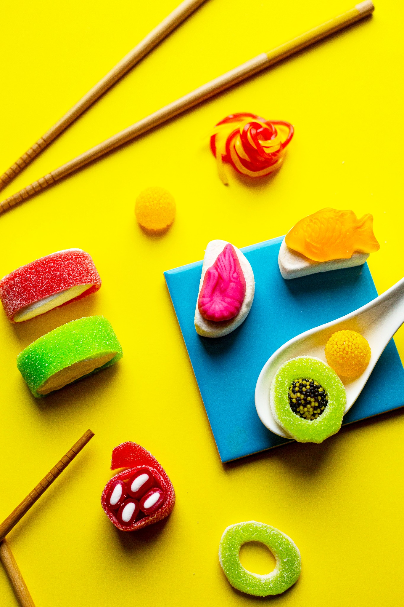 Żółte tło z kolorowymi cukierkami w kształcie sushi, ułożonymi obok pałeczek do jedzenia, prezentacja słodkich przysmaków w Warszawie.