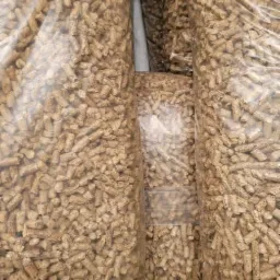 Foliowe worki wypełnione jasnobrązowym pelletem drzewnym, ułożone jeden obok drugiego.