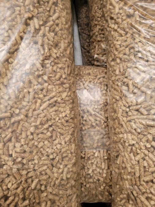 Foliowe worki wypełnione jasnobrązowym pelletem drzewnym, ułożone jeden obok drugiego.