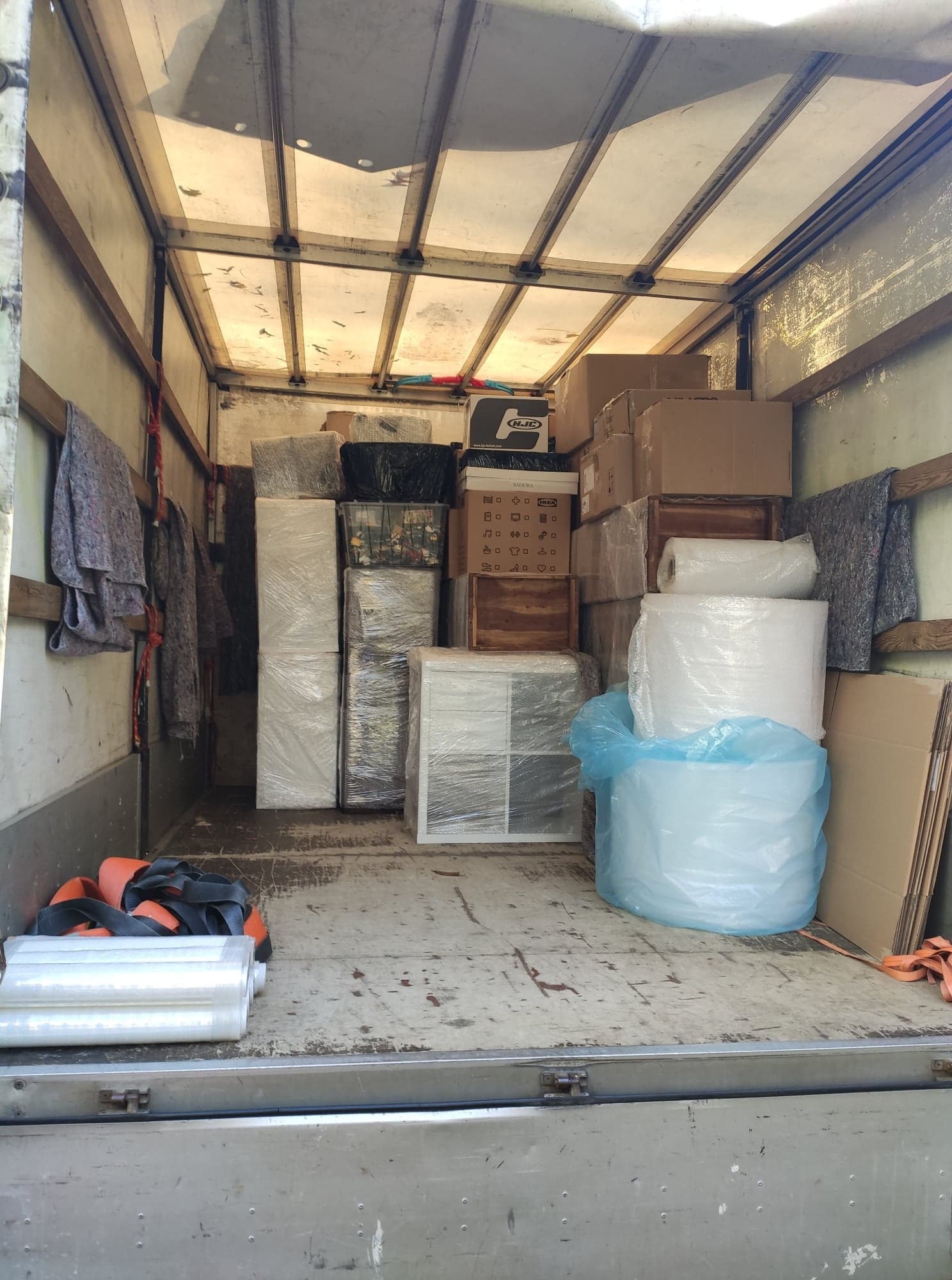 Wnętrze samochodu dostawczego wypełnione kartonami, meblami owiniętymi folią stretch i bąbelkową, zabezpieczonymi pasami transportowymi, gotowymi do przewozu.