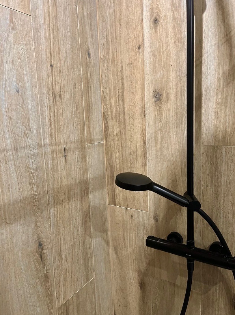 Kabina prysznicowa z czarną armaturą i okładziną ścienną imitującą drewno, widok z bliska na słuchawkę prysznicową.