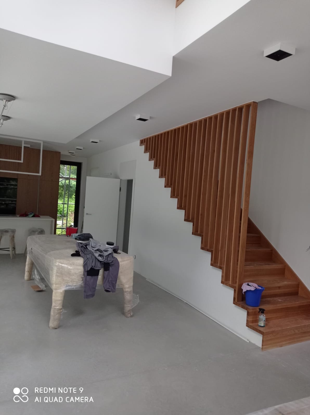 Jasne wnętrze w trakcie prac: zabezpieczone meble folią, drewniane schody z ażurową balustradą, świeżo pomalowane białe ściany i sufit z czarnymi punktami świetlnymi.