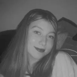 Portret młodej kobiety z długimi włosami, lekko uśmiechniętej, w czarno-białej tonacji, z delikatnym makijażem ust.